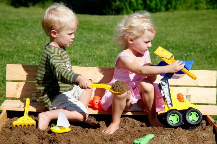 Zwei Kinder spielen in einem Sandkasten mit Schaufeln.